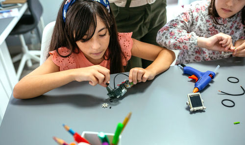 Student screwing electrical circuit next to her teacher and to schoolchild in robotics class