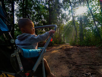 Rear view of boy sitting on land in forest