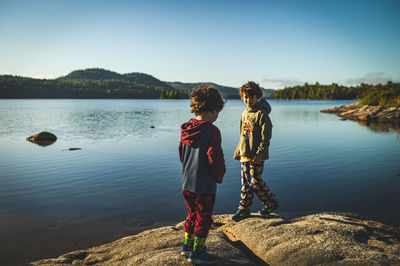 Two boys standing by lake against sky