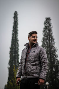 Young man looking away against trees