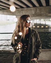 Portrait of young woman standing against illuminated wall at night