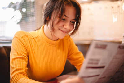 Happy teenage girl looking at menu while sitting in cafe