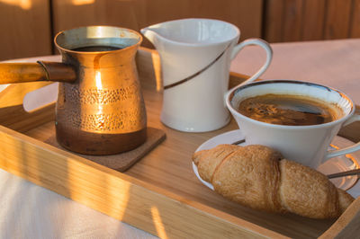 Breakfast is served on a wooden tray with copper pots, a cup of coffee and croissants sunlight 