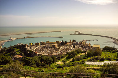 Aerial view of townscape and trees by sea against sky