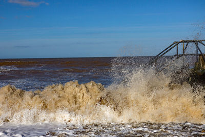 Sea waves splashing on shore against sky
