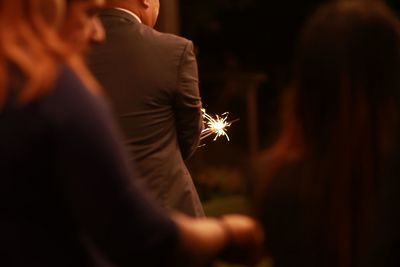 Man holding lit sparkler against sky at night