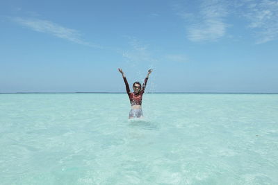 Man with arms raised standing in sea against sky