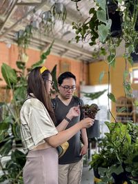 Young asian man and woman having a discussion as they choose potted plants inside plant nursery.