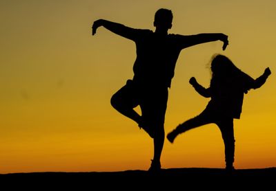 Silhouette couple standing on field against sky during sunset