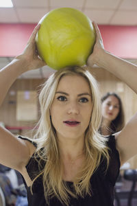 A young woman holding a bowling ball on top of her head.