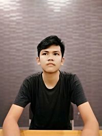 Young man looking away while sitting against wall