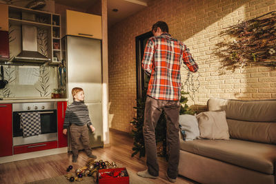 Rear view of man standing on sofa at home