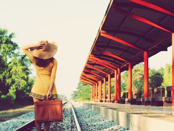 Rear view of woman standing on railroad track by station against sky