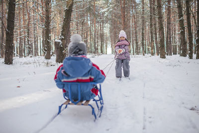 Happy friends have fun in wonderland, girl pulls sledge with sister and brother across winter forest