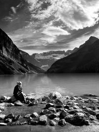 Man sitting on rock by lake against sky