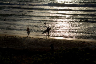 Silhouette people standing at beach during sunset