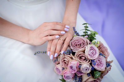 The bride's hands next to the bouquet on the background of the wedding dress