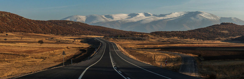 Road leading towards snowy mountains against sky in anatolian arid landscape