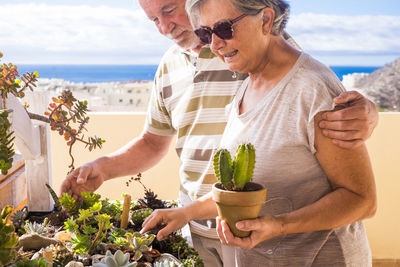 Smiling senior couple holding plants standing outdoors