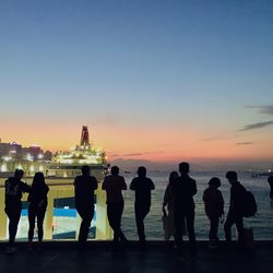 Silhouette people standing by sea against sky during sunset