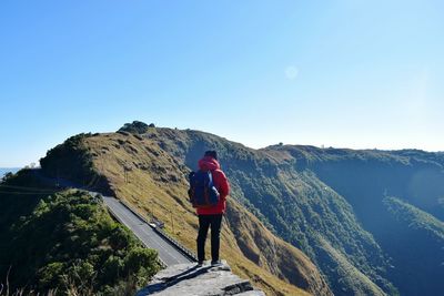 Rear view of woman standing on mountain against clear blue sky