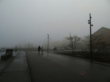 People walking on road against sky during foggy weather