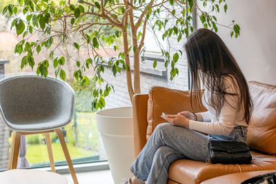 A young girl with a phone in her hands is sitting on the couch.