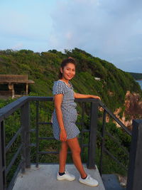 Portrait of woman standing on railing against sky