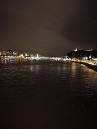 Illuminated city by sea against sky at night