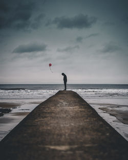 Man standing on pier at beach against sky