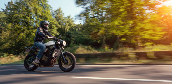 Man riding motorcycle on road against trees