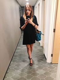 Full length of young woman using phone while standing on tiled floor