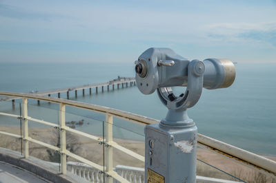 Close-up of coin-operated binoculars by railing against sky