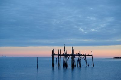 Wooden posts in sea against cloudy sky at sunset