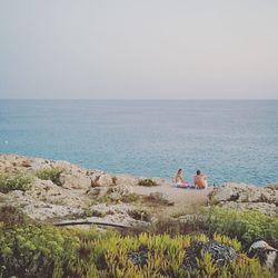 People sitting on shore by sea against sky