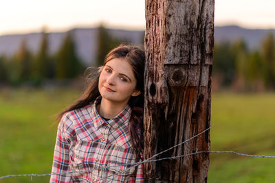 Portrait of  young woman standing by fence post