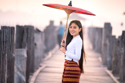 Portrait of smiling woman with umbrella standing on footpath