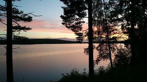 Silhouette trees by lake against sky during sunset