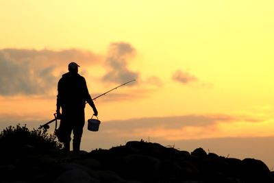 Silhouette man standing on rock against sky during sunset