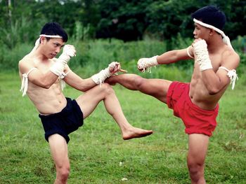 Shirtless male fighters practicing on grass against sky