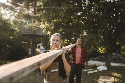 Heterosexual couple carrying wooden plank in backyard