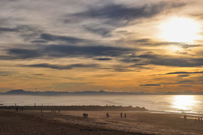 Silhouette people on beach against sky during sunset