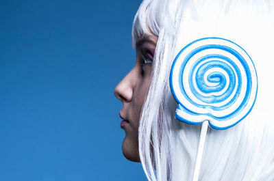 Side view close-up of woman with lollipop against blue background