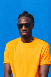 Portrait of young man wearing sunglasses standing against blue wall