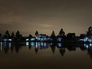 Silhouette buildings by lake against sky at night