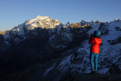 Rear view of person standing on snowcapped mountain against sky