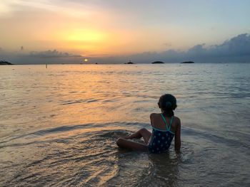 Rear view of girl playing in sea against sky during sunset
