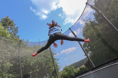 Low angle view of woman jumping on tree against sky