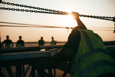 Rear view of silhouette man by railing against sky during sunset