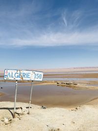 Sign board on beach against sky